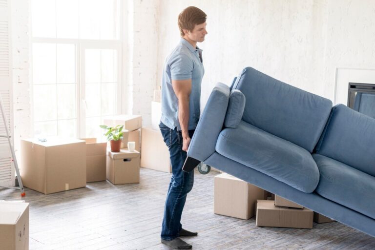 Hombre en una sala de estar cargando un sillón azul. Fondo de cajas de cartón apiladas Bodega Guadalajara